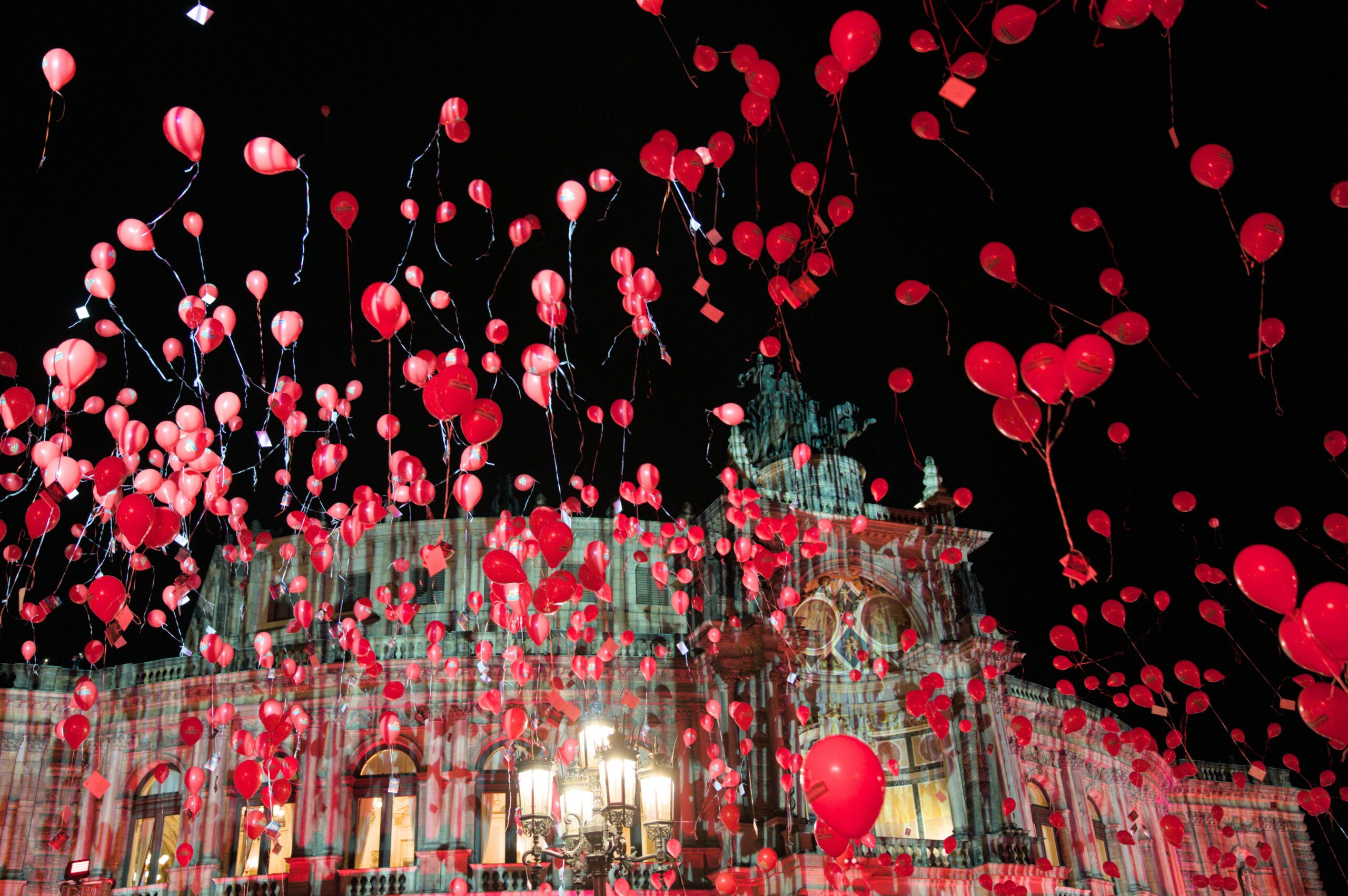 Hundreds of red balloons released into the night sky in front of a historic opera house, romantic celebration.